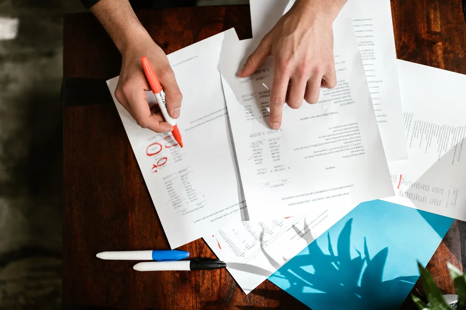 Mani controllano dati e importi su documenti aziendali, evidenziando le voci da verificare.